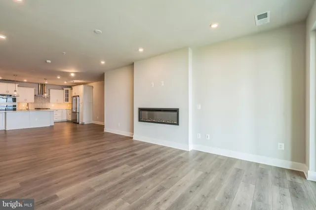 an empty room with wooden floor and kitchen view