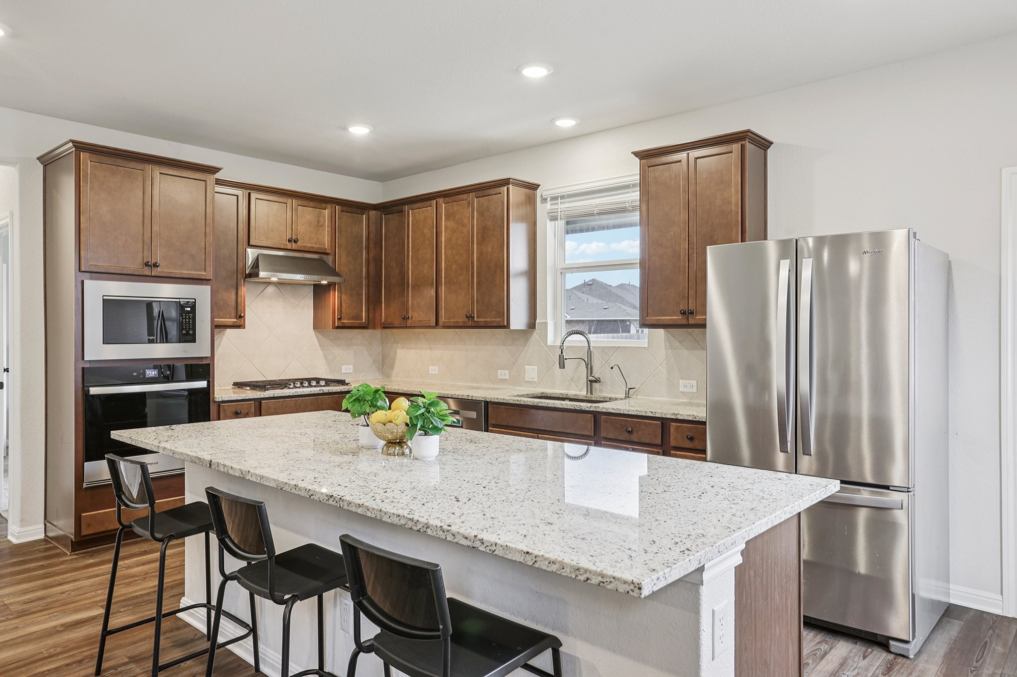 204 Swinging H Lane Georgetown, TX 78633 - Photo 5 of 39 This kitchen features rich wood cabinetry, a large kitchen island with a light-colored countertop, and stainless steel appliances including a refrigerator, microwave, and oven