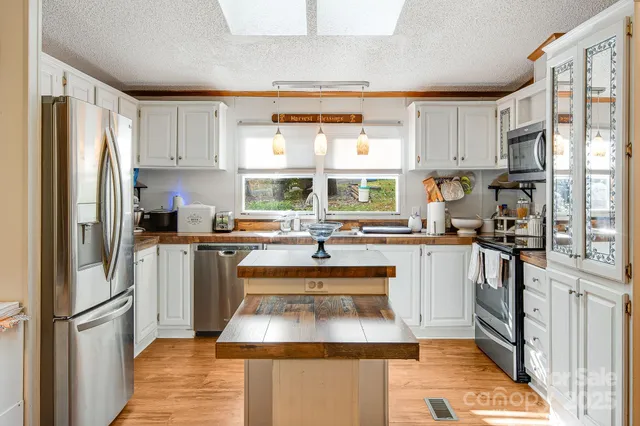 a kitchen with stainless steel appliances granite countertop a refrigerator a sink dishwasher a stove and white countertops with wooden floor