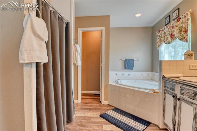 7863 Buschborn Road Peyton, CO 80831 - Photo 21 of 50 Bathroom with tiled tub, vanity, and hardwood / wood-style flooring