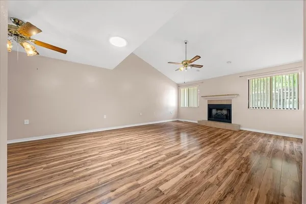 a view of an empty room with wooden floor fireplace and a window