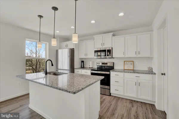 a kitchen with stainless steel appliances granite countertop a sink a stove a refrigerator and white cabinets with wooden floor