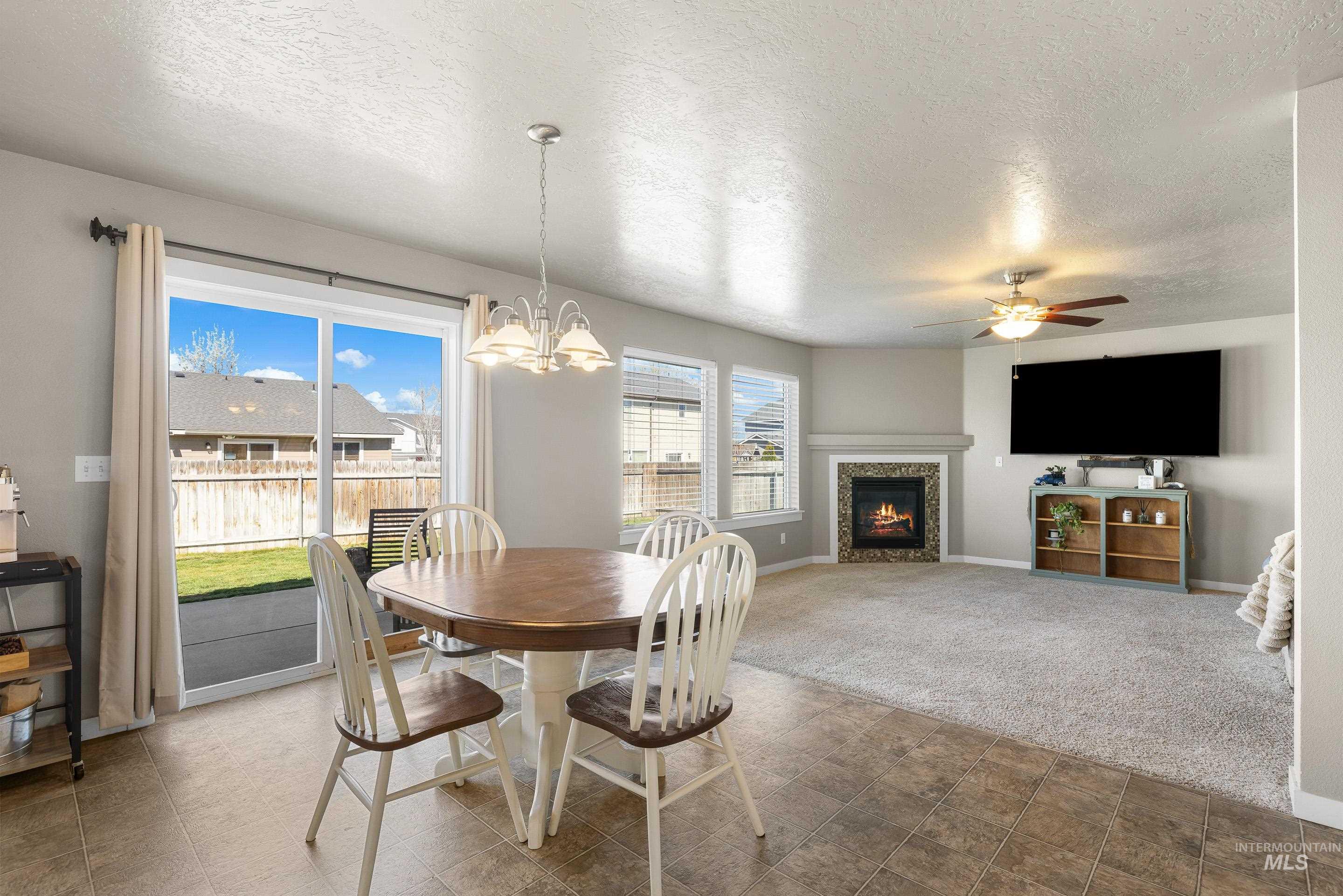 700 Southwest Panner Street Mountain Home, ID 83647 - Photo 13 of 50 Carpeted dining room with a warm lit fireplace, a textured ceiling, hanging lights, and ceiling fan