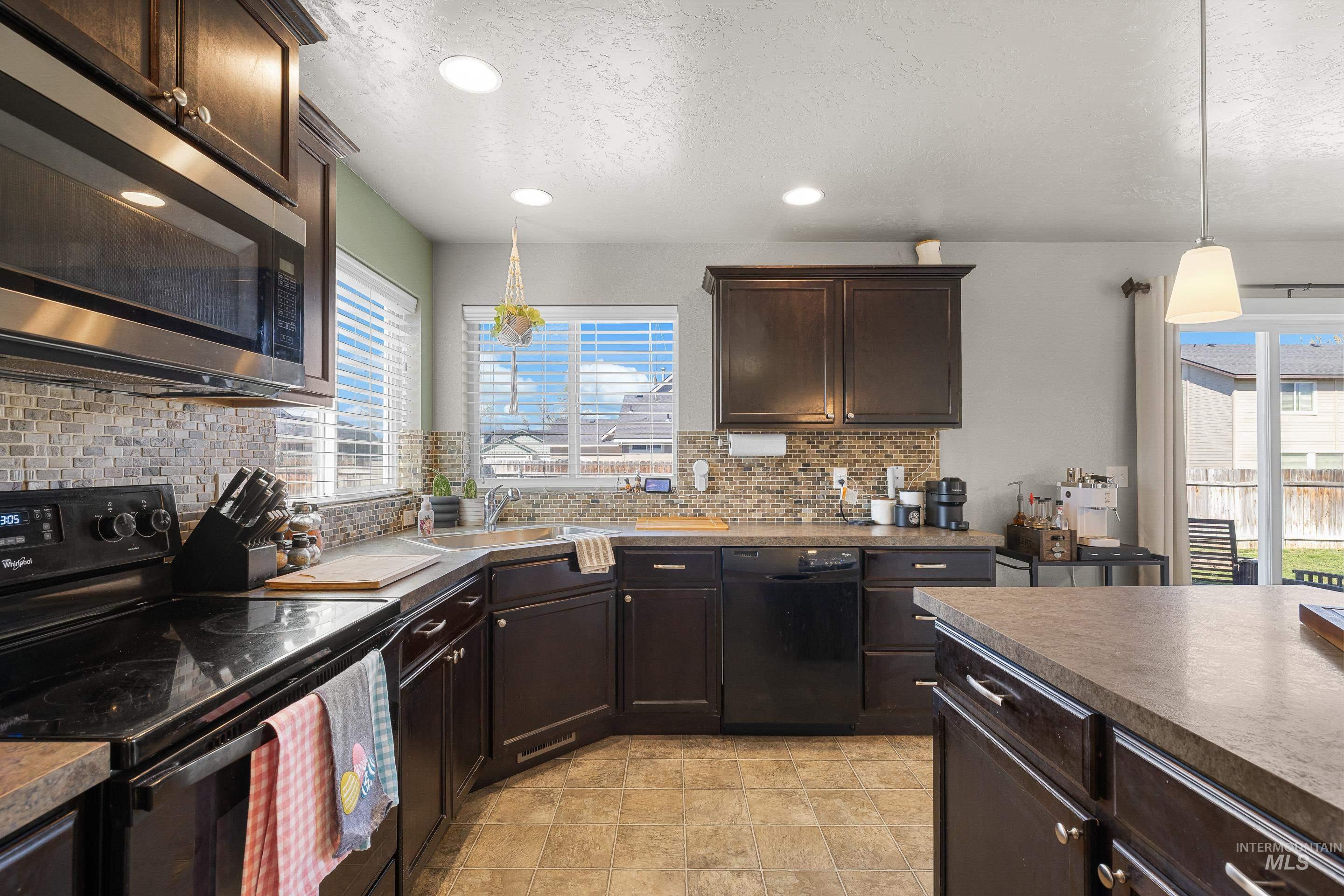 700 Southwest Panner Street Mountain Home, ID 83647 - Photo 15 of 50 Kitchen with black appliances, dark wood finish cabinets, hanging light fixtures, dark countertops, and a textured ceiling