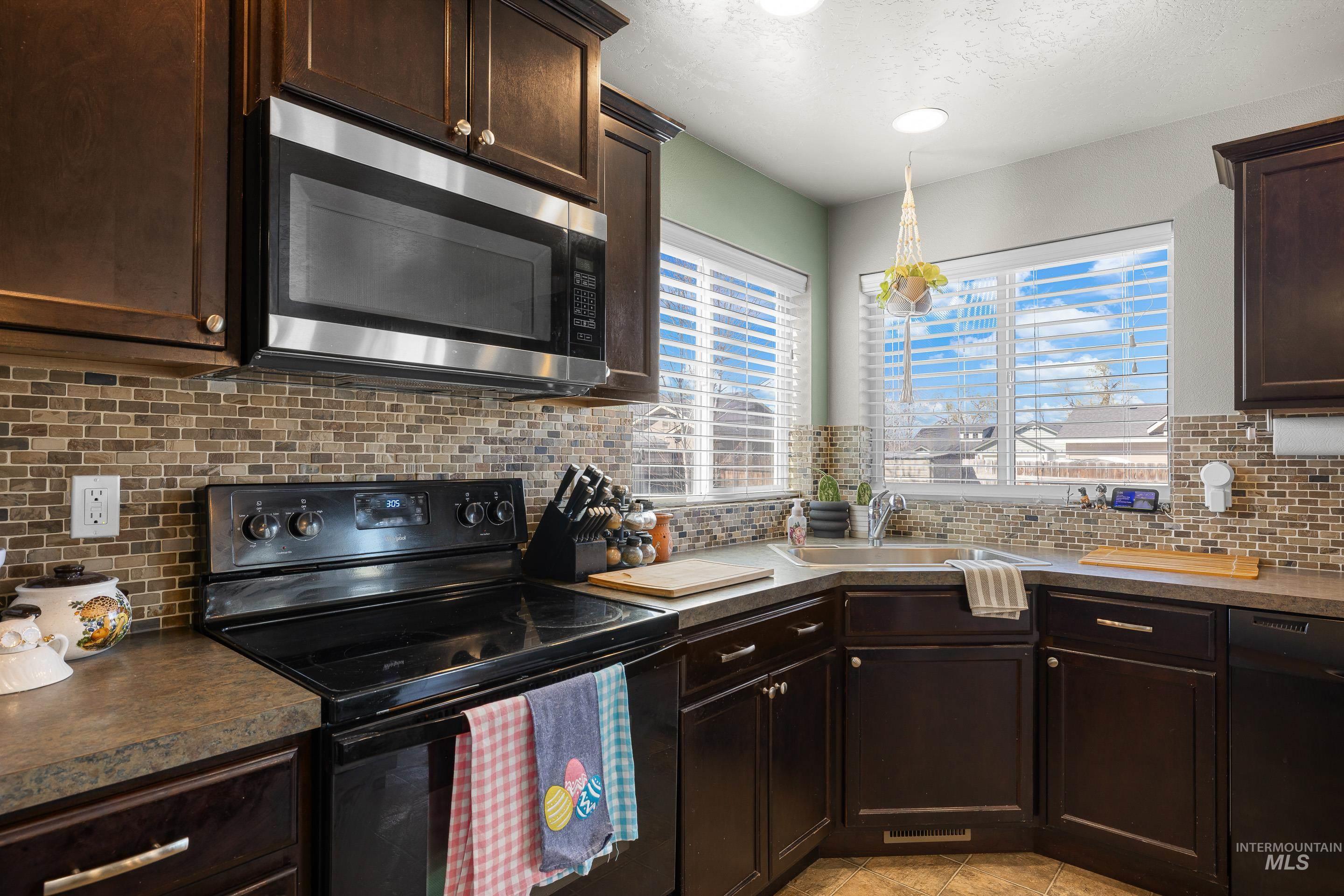 700 Southwest Panner Street Mountain Home, ID 83647 - Photo 16 of 50 Kitchen with black appliances, dark wood finish cabinetry, tasteful backsplash, light tile patterned flooring, and a textured ceiling