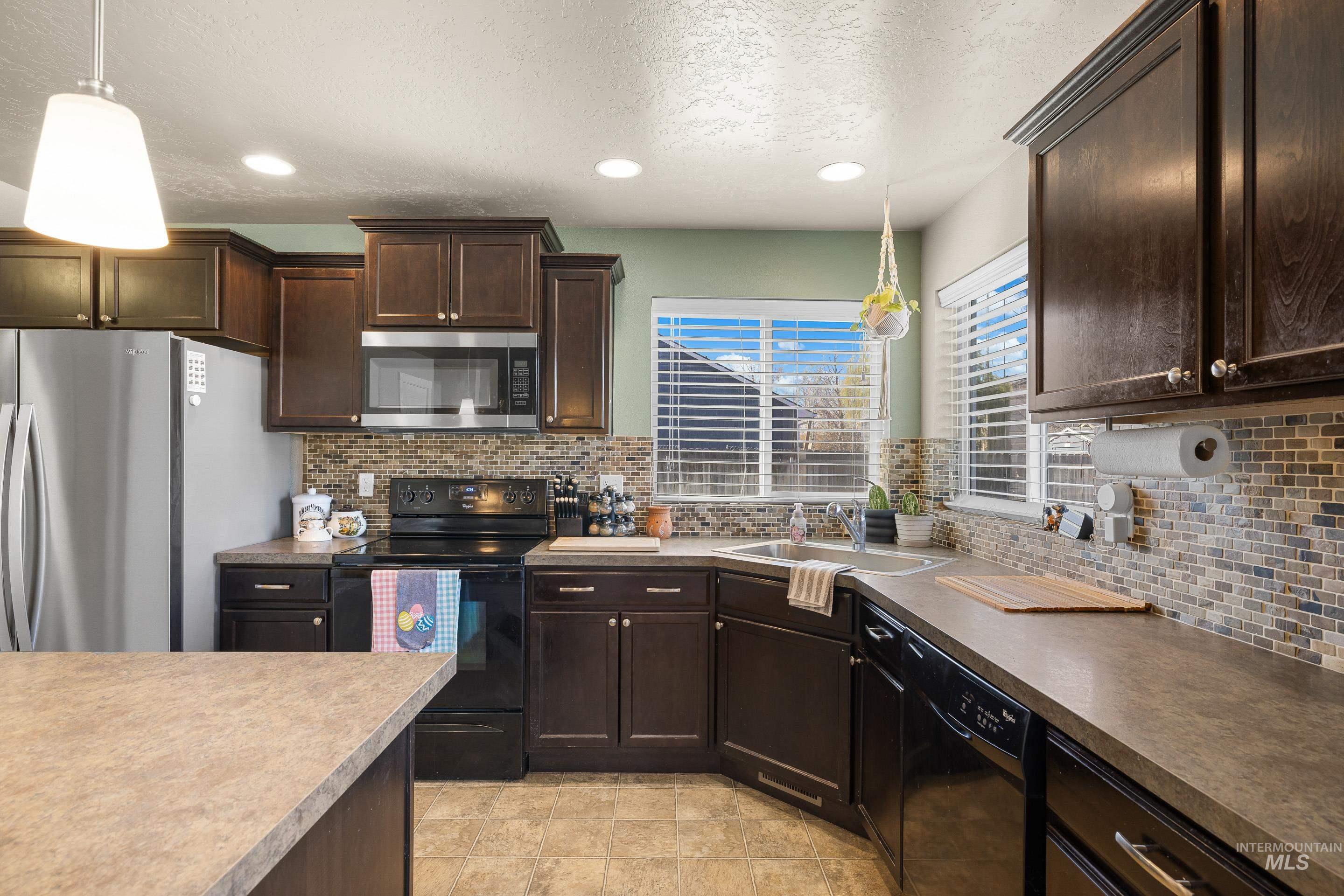 700 Southwest Panner Street Mountain Home, ID 83647 - Photo 18 of 50 Kitchen featuring dark wood finish cabinets, black appliances, hanging light fixtures, a textured ceiling, and backsplash