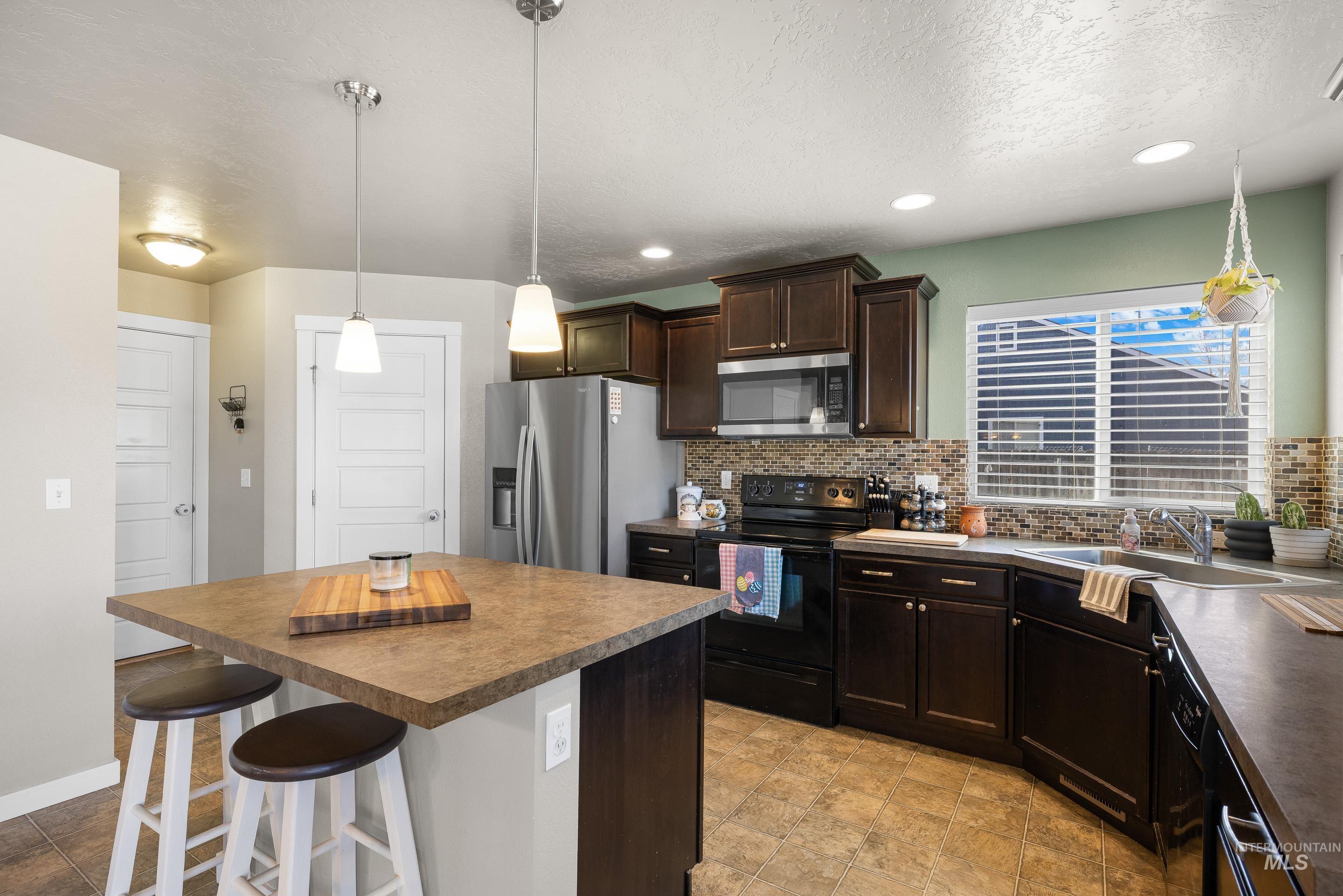 700 Southwest Panner Street Mountain Home, ID 83647 - Photo 19 of 50 Kitchen featuring black appliances, dark wood finish cabinetry, a kitchen bar, a kitchen island, and pendant lighting