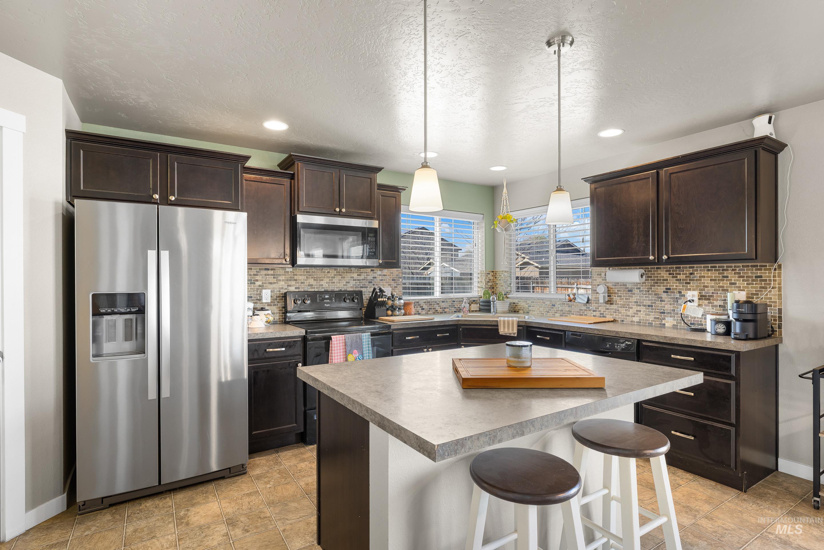 700 Southwest Panner Street Mountain Home, ID 83647 - Photo 20 of 50 Kitchen featuring stainless steel appliances, dark wood finish cabinets, a breakfast bar area, a kitchen island, and a textured ceiling