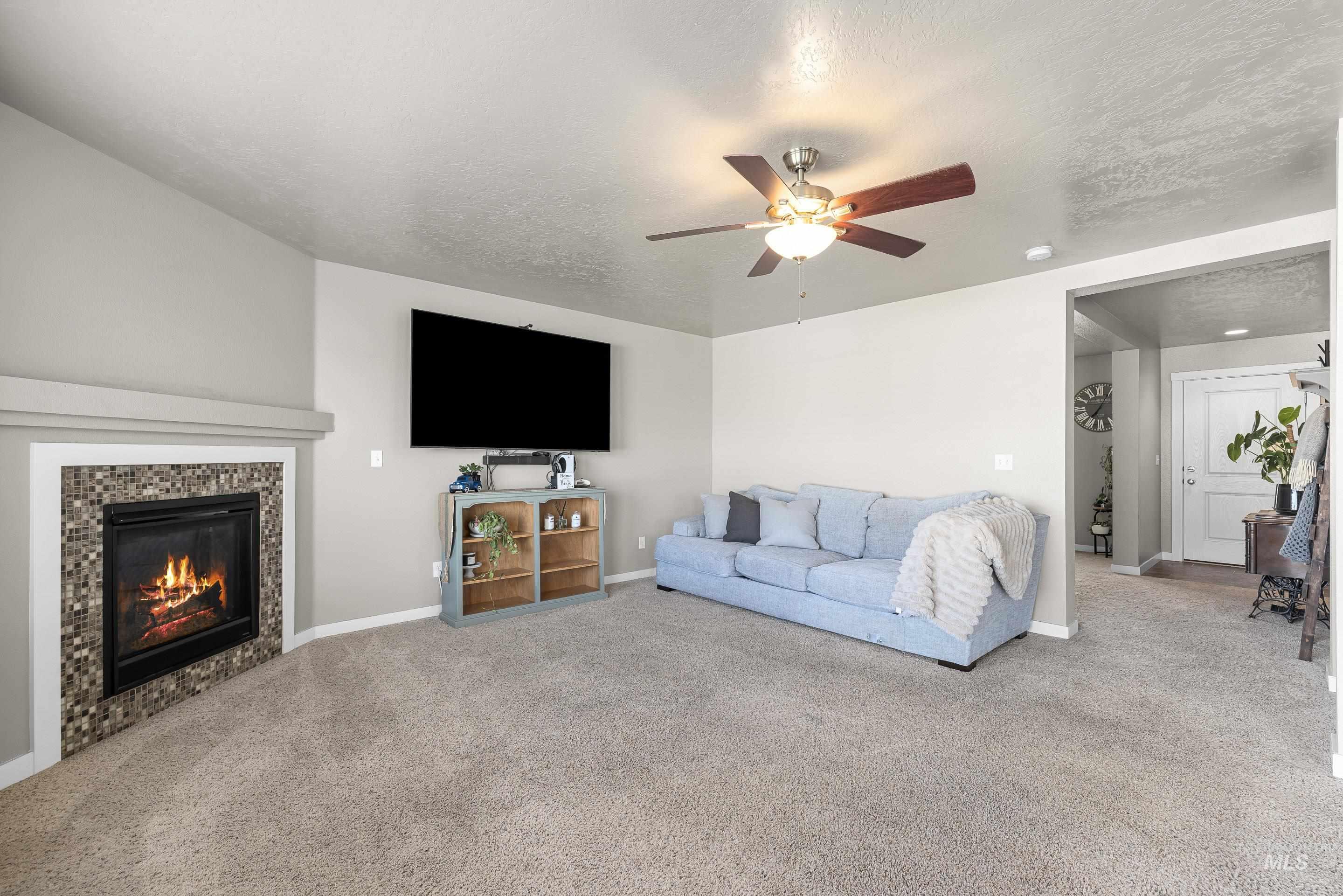 700 Southwest Panner Street Mountain Home, ID 83647 - Photo 6 of 50 Carpeted living room with ceiling fan, a textured ceiling, and a tiled fireplace