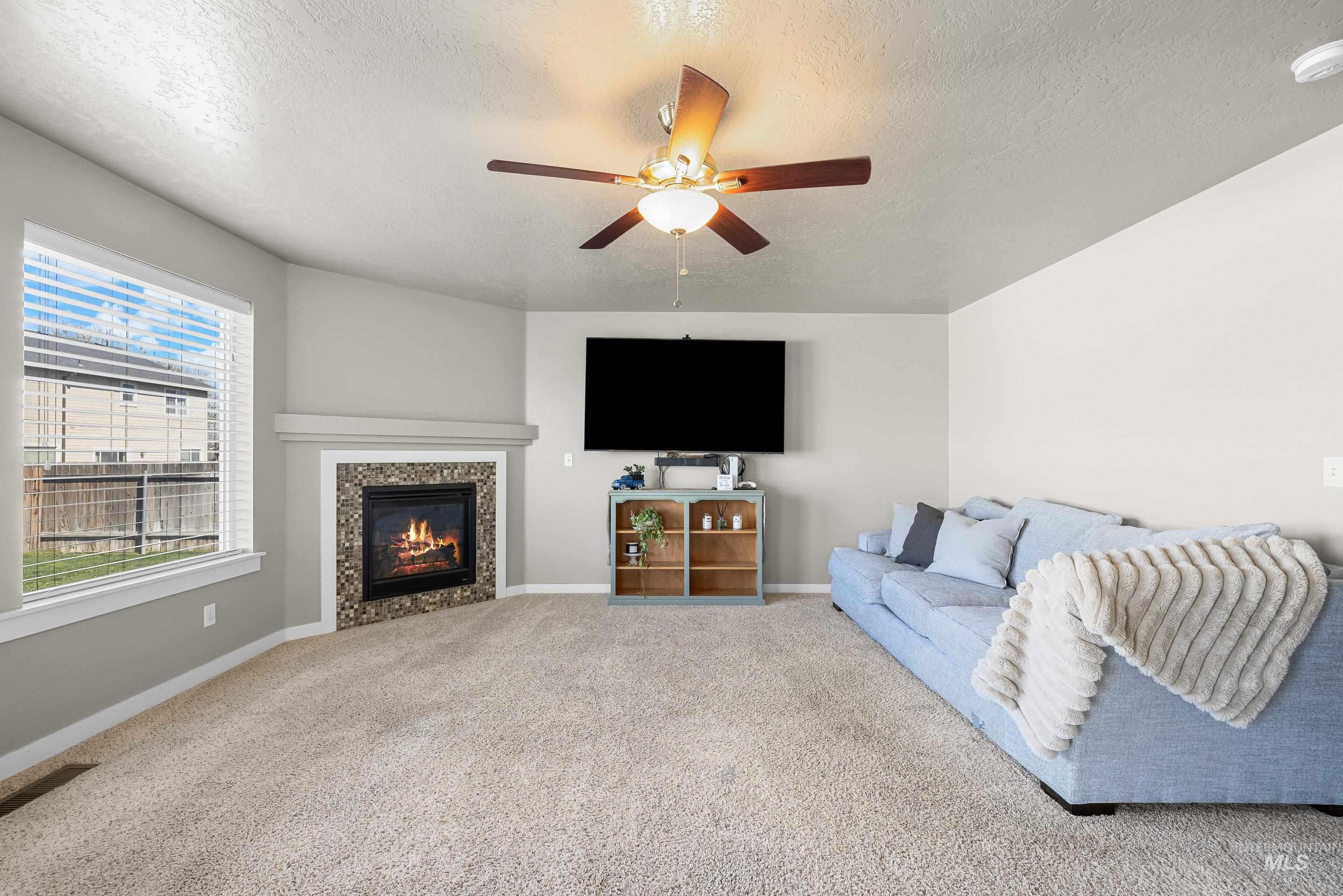 700 Southwest Panner Street Mountain Home, ID 83647 - Photo 7 of 50 Carpeted living room featuring a tile fireplace, a textured ceiling, and a ceiling fan