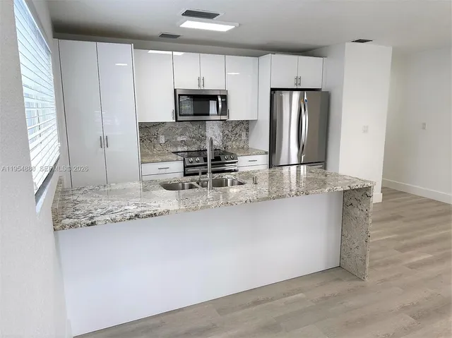 a kitchen with granite countertop a sink a stove a microwave a refrigerator and white cabinets