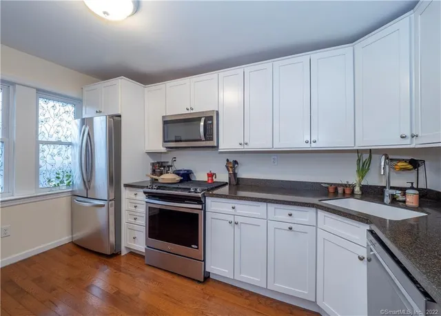 a kitchen with stainless steel appliances granite countertop white cabinets a sink a stove a refrigerator and microwave with wooden floor