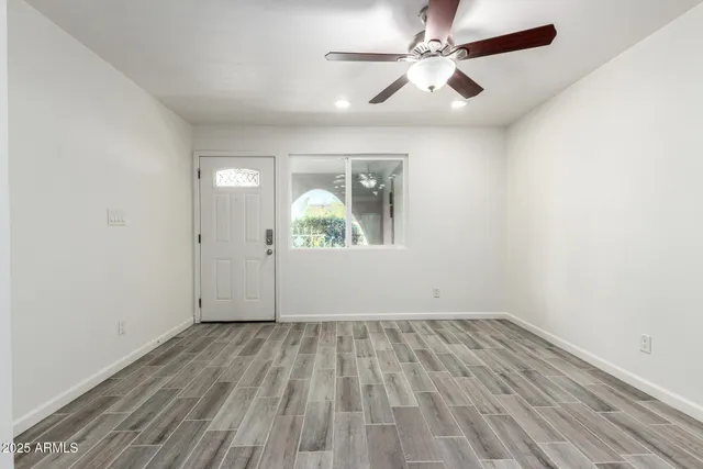 an empty room with wooden floor chandelier fan and windows