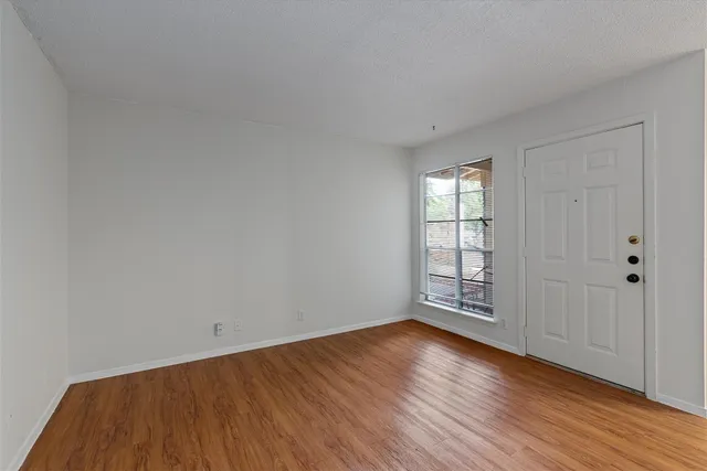 a view of an empty room with wooden floor and window