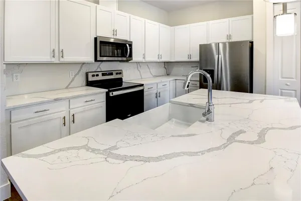 a kitchen with granite countertop a refrigerator sink and white cabinets