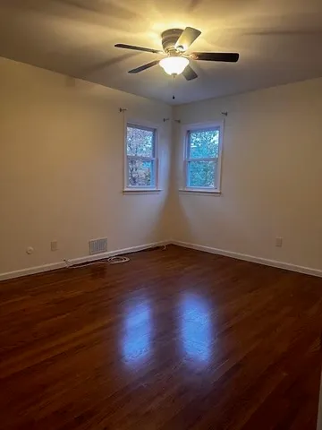 an empty room with wooden floor chandelier fan and windows