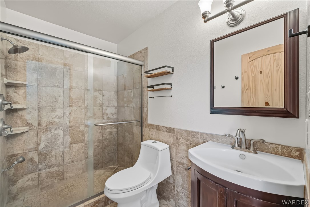 4088 Mercer Road Bullhead City, AZ 86429 - Photo 18 of 35 Bathroom featuring a walk-in shower with tiled walls and glass enclosure, a white toilet, and a vanity with a curved sink