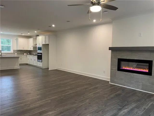 an empty room with wooden floor fireplace and kitchen view