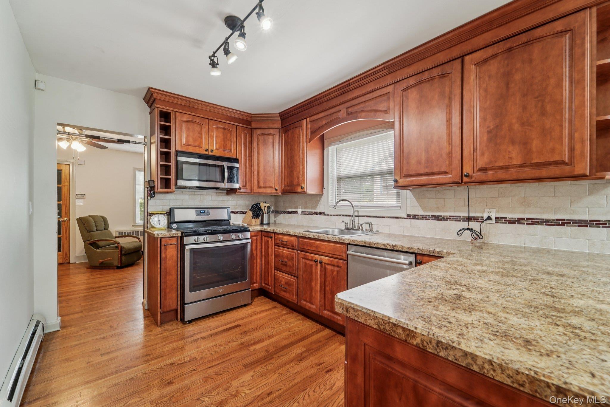10 Ward Street Suffern, NY 10901 - Photo 13 of 34 Kitchen featuring appliances with stainless steel finishes, open shelves, baseboard heating, light wood-style flooring, and decorative backsplash