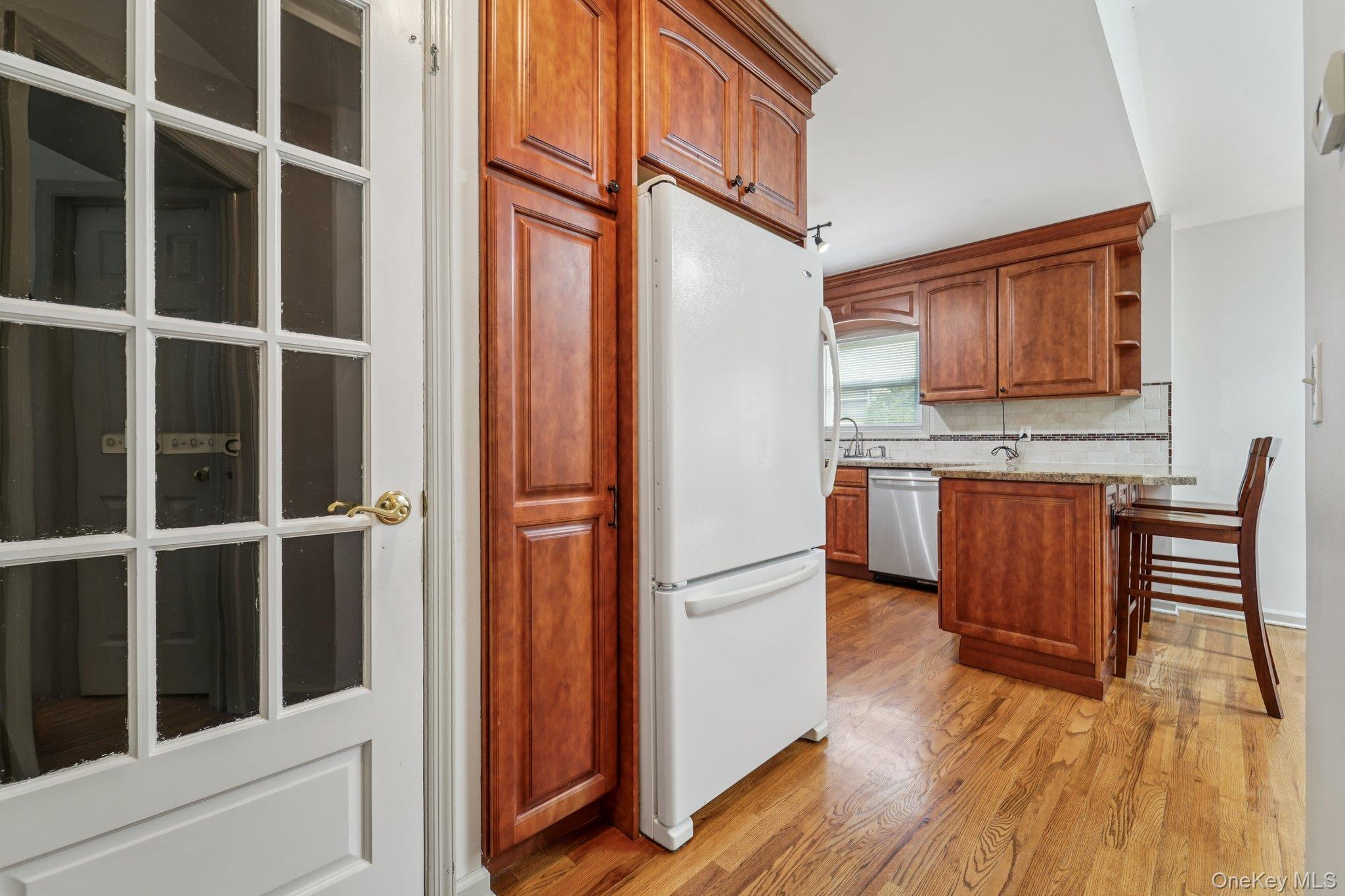 10 Ward Street Suffern, NY 10901 - Photo 14 of 34 Kitchen featuring freestanding refrigerator, stainless steel dishwasher, light wood-style floors, brown cabinetry, and a breakfast bar
