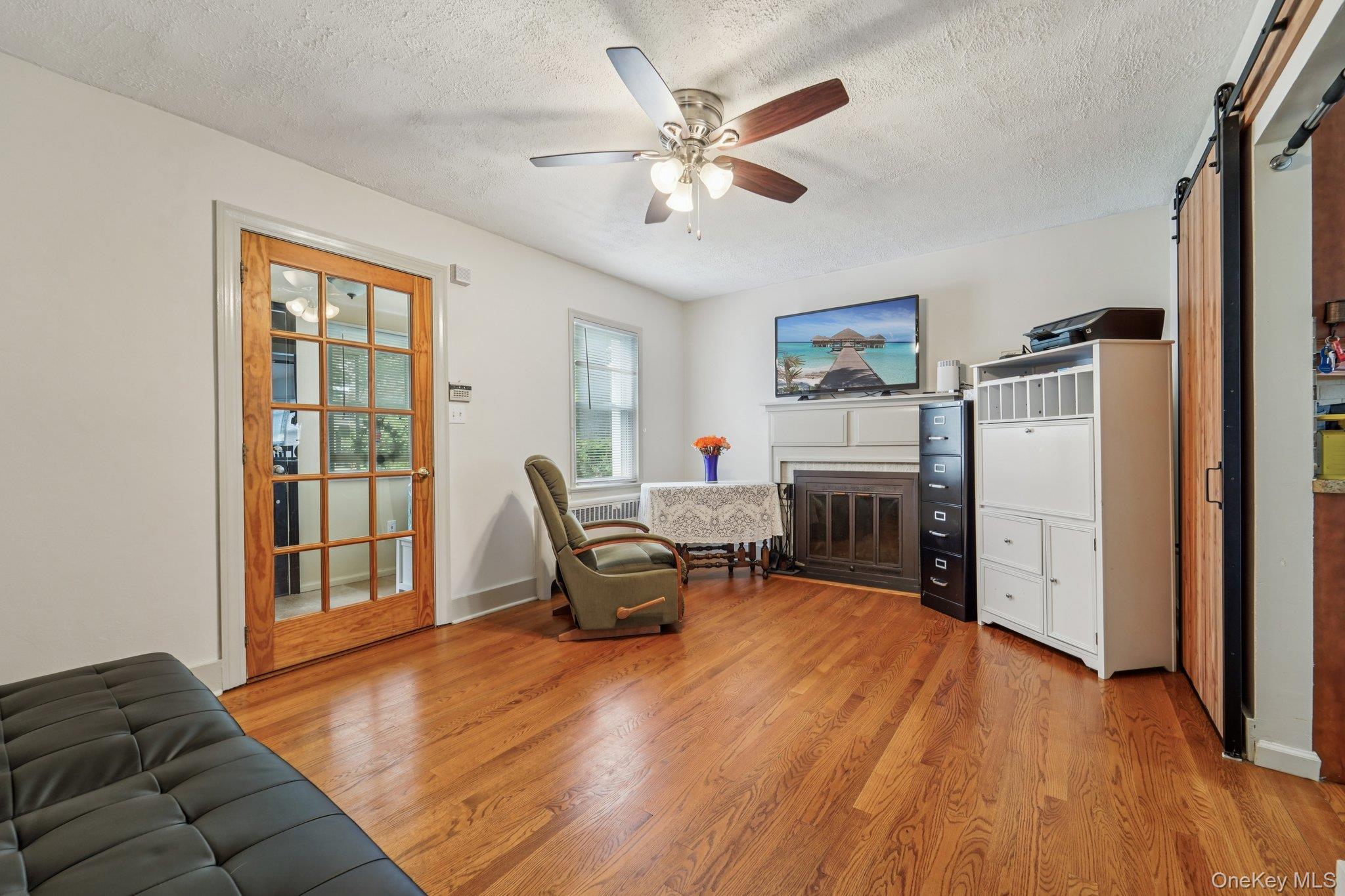 10 Ward Street Suffern, NY 10901 - Photo 6 of 34 Living area with light wood-style floors, a barn door, a textured ceiling, ceiling fan, and a glass covered fireplace