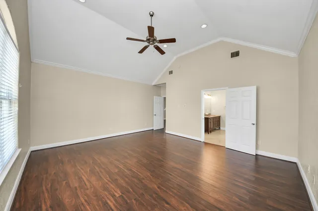 an empty room with wooden floor ceiling fan and windows