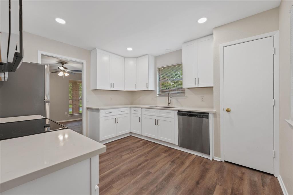 4005 Ridgebrook Drive Arlington, TX 76015 - Photo 8 of 18 Kitchen featuring wood-finish flooring, white cabinetry with silver-tone hardware, light-toned countertops, a stainless steel dishwasher, and a window above the sink