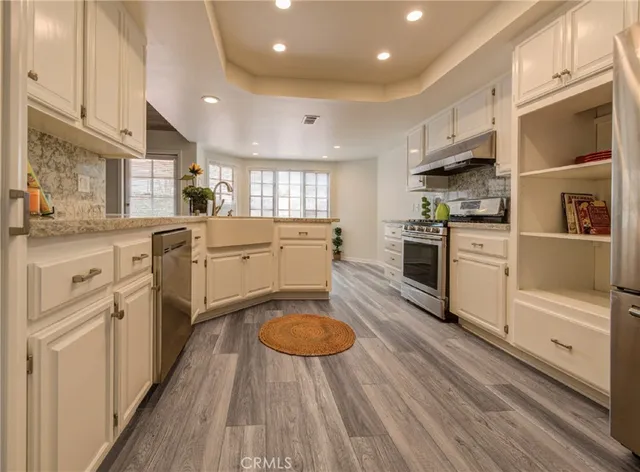 a kitchen with stainless steel appliances granite countertop a stove top oven a sink dishwasher and a refrigerator with wooden floor