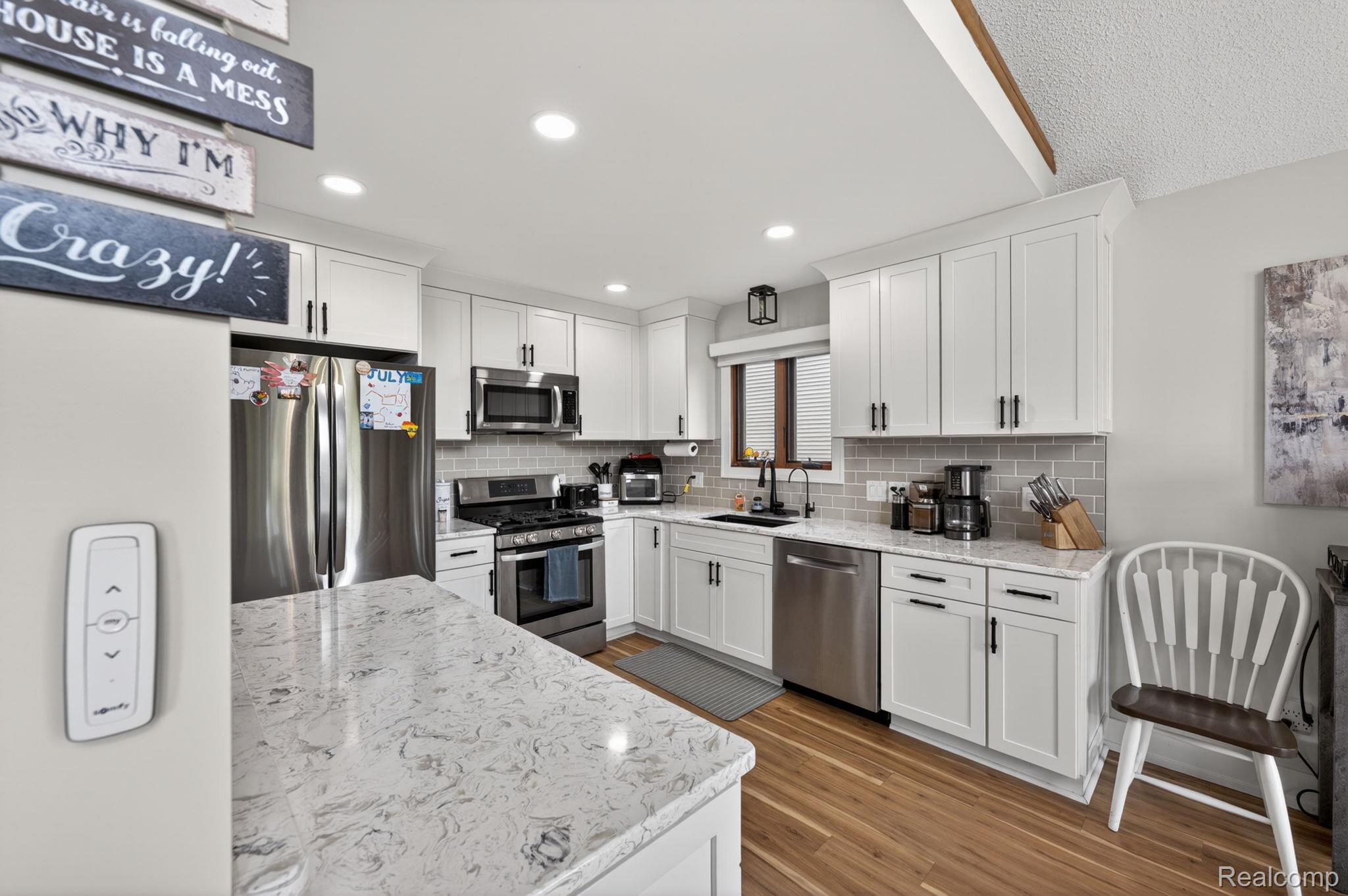 1280 Petts Road Fenton, MI 48430 - Photo 15 of 62 Kitchen featuring white cabinetry, stainless steel appliances, dark wood-style flooring, light stone counters, and decorative backsplash