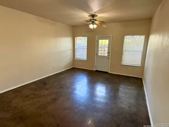 an empty room with wooden floor fan and windows