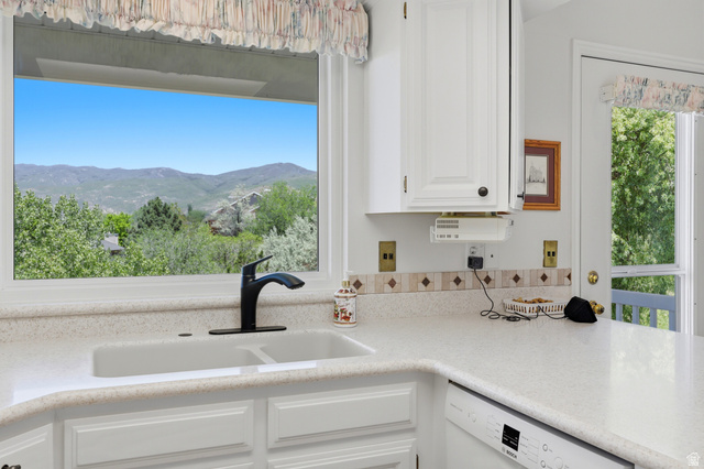 3766 Cardiff Circle Bountiful, UT 84010 - Photo 10 of 46 Kitchen window with a mountain backdrop, featuring a double basin sink, black faucet, light-colored countertops, and white cabinetry
