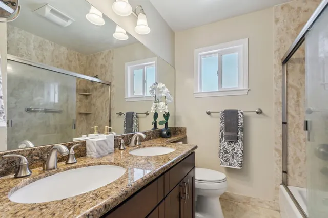 a bathroom with a granite countertop double vanity sink a mirror and a toilet