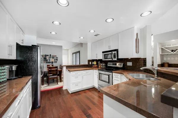 a kitchen with stainless steel appliances granite countertop a stove top oven a sink a dining table and chairs with wooden floor