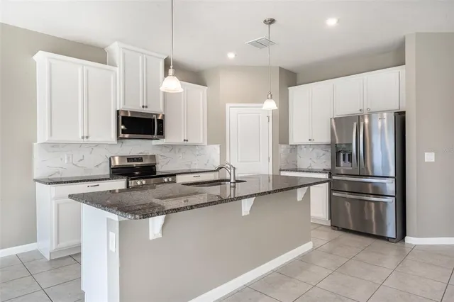 a kitchen with stainless steel appliances granite countertop a refrigerator a stove a sink a microwave and white cabinets