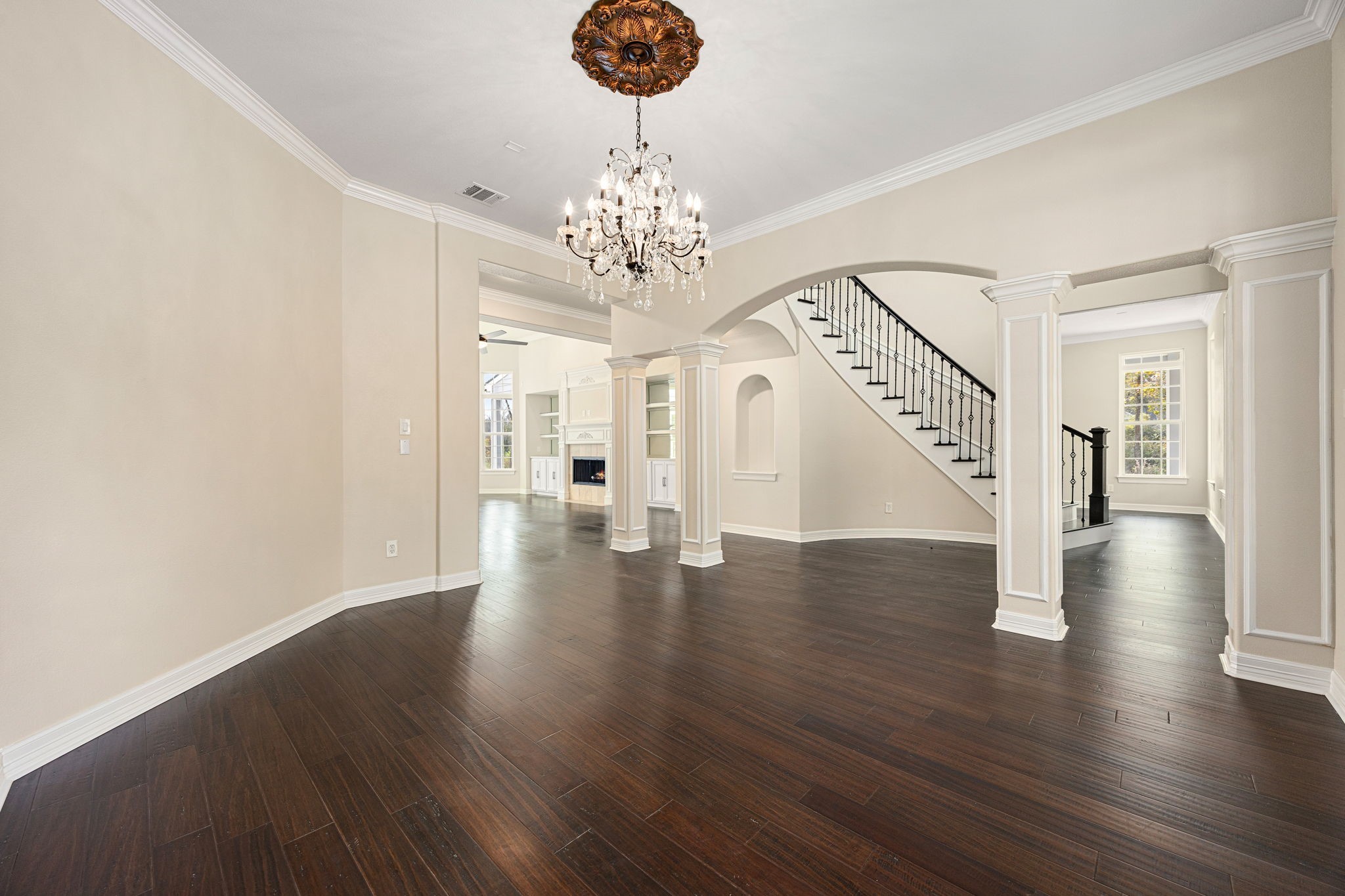 14882 Gingham Road Montgomery, TX 77356 - Photo 8 of 41 This elegant space features dark hardwood floors, a stunning chandelier, and a grand staircase with iron railings. The open layout connects to a well-lit living area with built-in shelving and a fireplace, offering a luxurious ambiance.