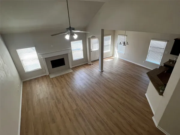 a view of an empty room with wooden floor and a kitchen