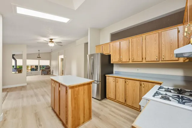 a kitchen with stainless steel appliances granite countertop a refrigerator a sink dishwasher a stove and white countertops with wooden floor