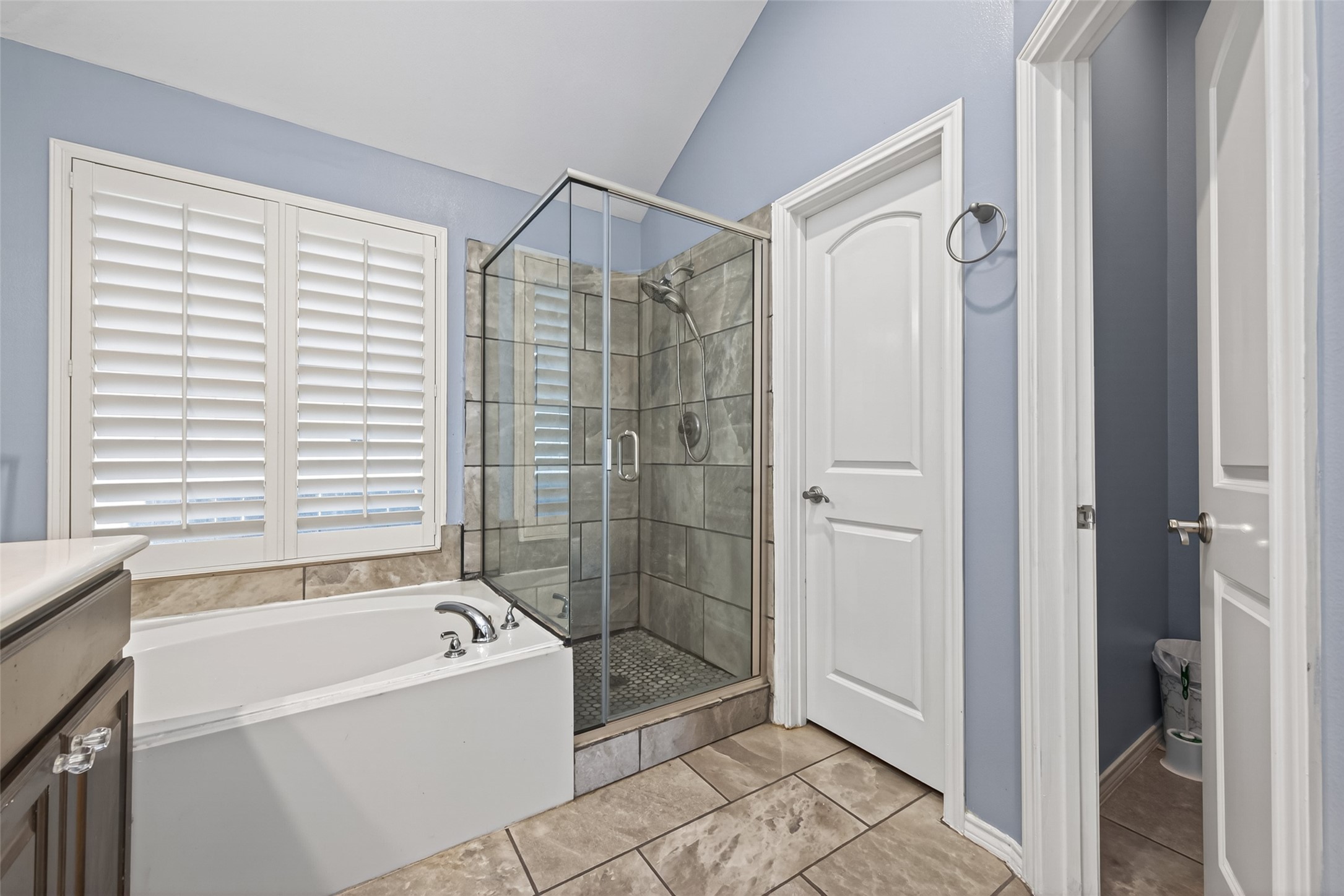 27443 Rebecca Field Lane Spring, TX 77386 - Photo 19 of 31 This bathroom features a modern design with a glass-enclosed shower, a separate bathtub, and stylish tile flooring. It has a soothing color palette and ample natural light from a window with plantation shutters.