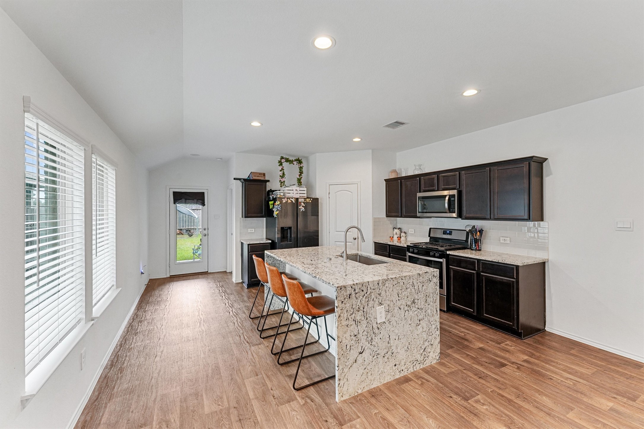 22411 Gilded Peak Lane Spring, TX 77373 - Photo 2 of 16 a kitchen with stainless steel appliances kitchen island granite countertop a stove top oven a sink dishwasher a dining table and chairs with wooden floor