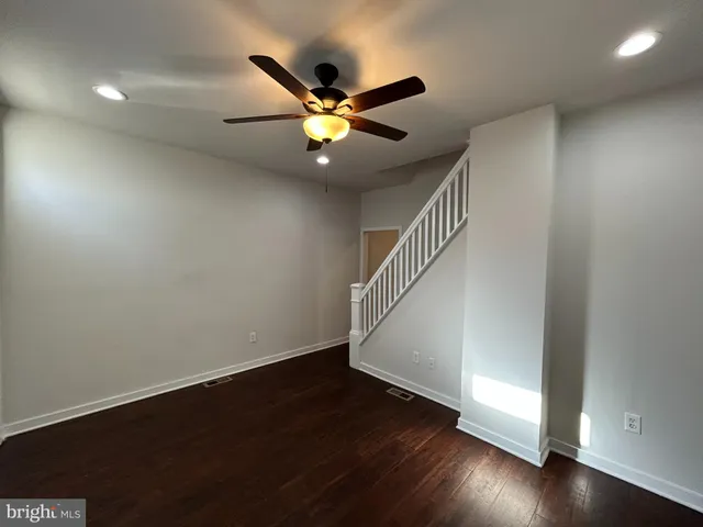 a view of an empty room with wooden floor and a ceiling fan