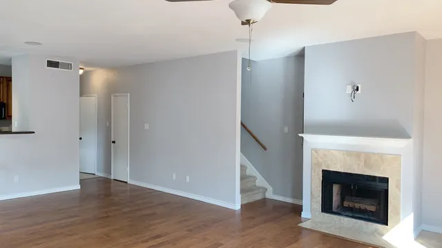 a view of an empty room with wooden floor fireplace and a window
