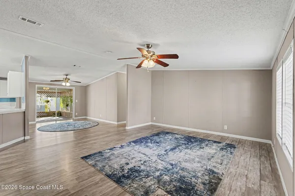 a view of an empty room and kitchen with wooden floor