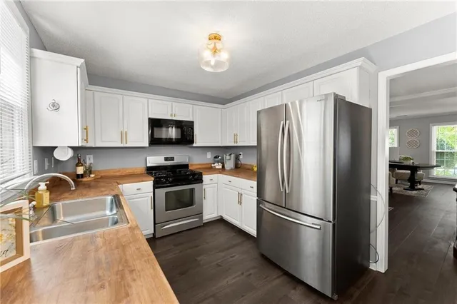 a kitchen with stainless steel appliances granite countertop a refrigerator a stove a sink a microwave and a dining table with wooden floor