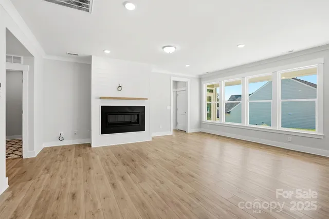 a view of an empty room with wooden floor fireplace and a window