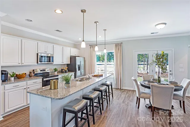 a kitchen with stainless steel appliances granite countertop a stove a refrigerator a kitchen island a dining table and chairs with wooden floor