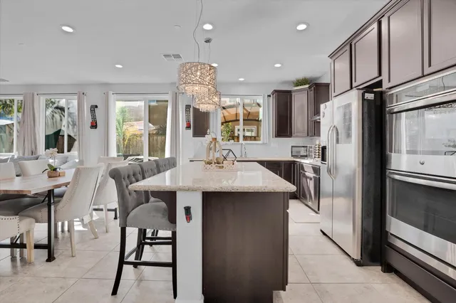 a kitchen with stainless steel appliances kitchen island granite countertop a table chairs and a refrigerator