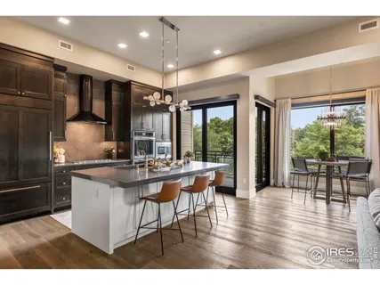 a kitchen with stainless steel appliances granite countertop a stove top oven a refrigerator a dining table and chairs with wooden floor