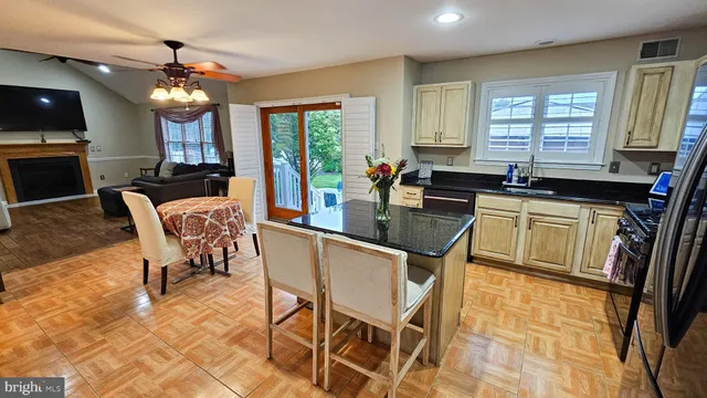 a dining hall with stainless steel appliances granite countertop a stove a kitchen island a dining table and chairs with wooden floor