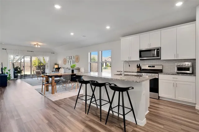 a kitchen with stainless steel appliances granite countertop a stove a sink a microwave a dining table and chairs with wooden floor