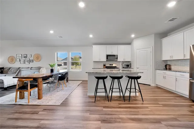a kitchen with stainless steel appliances kitchen island granite countertop a table chairs sink and cabinets